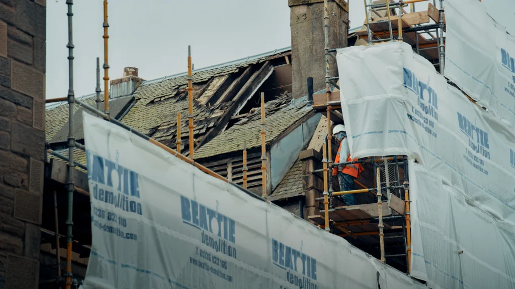 Brick building under facade repair with scaffolding, protective sheeting and a worker on site
